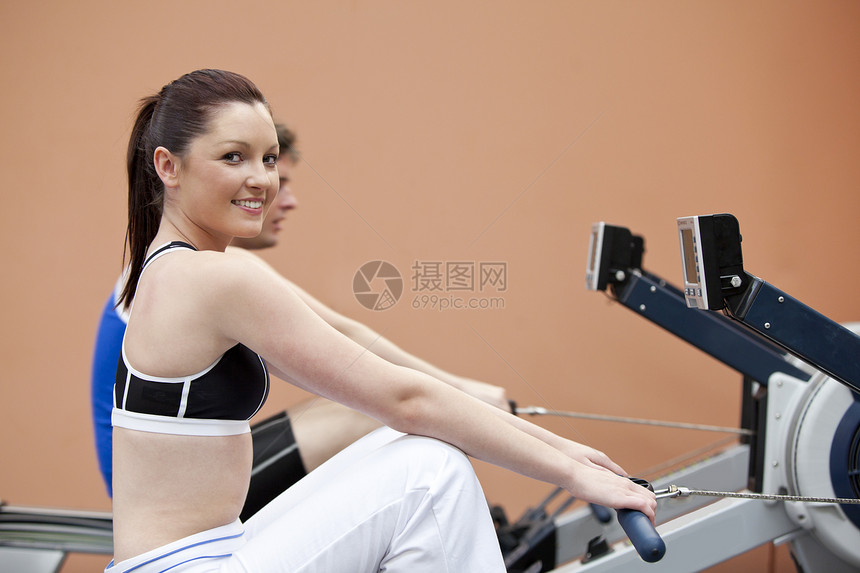 快乐的女子与男朋友 在健身中心用划轮机图片