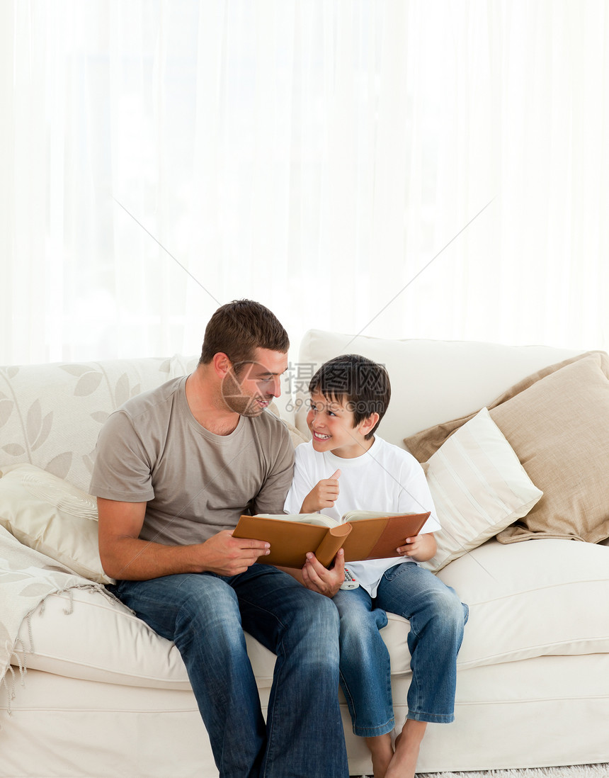 可爱的男孩在看相册时 和他父亲一起坐在沙发上图片