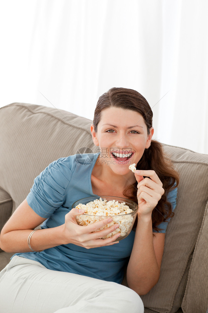 一个快乐的女子在看电视的同时吃流行玉米的肖像图片