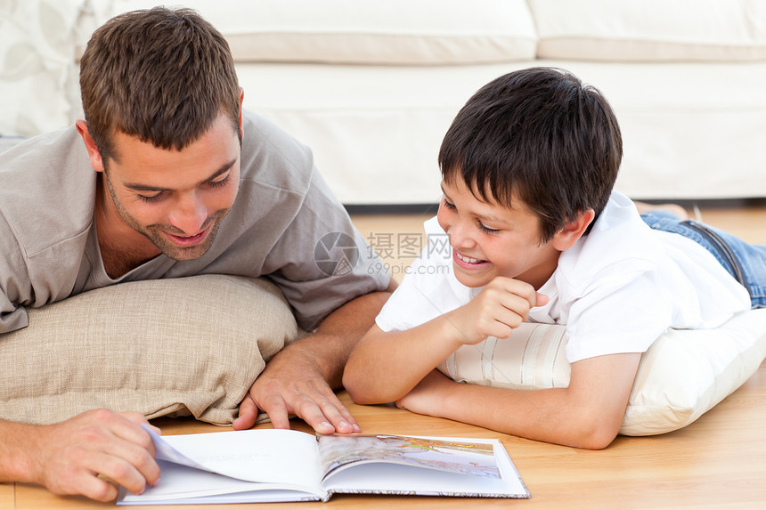 快乐的父亲和儿子一起在地板上阅读一本书图片