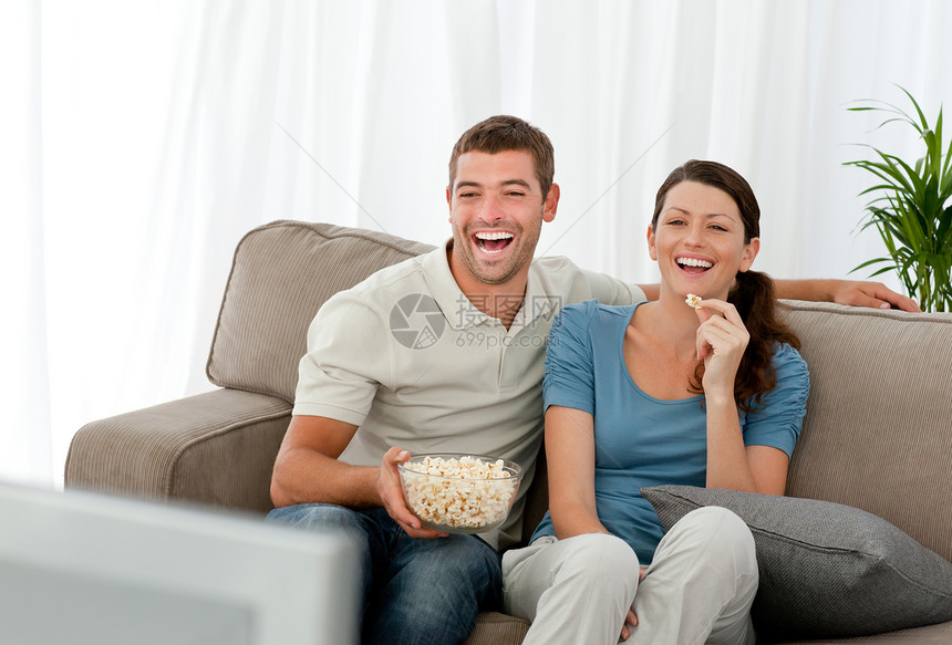 可爱的情侣在电视面前放松时笑着图片