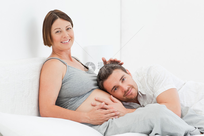 丈夫在听妻子的肚子说谎享受婴儿腹部爸爸情感女性父母几个月喜悦图片