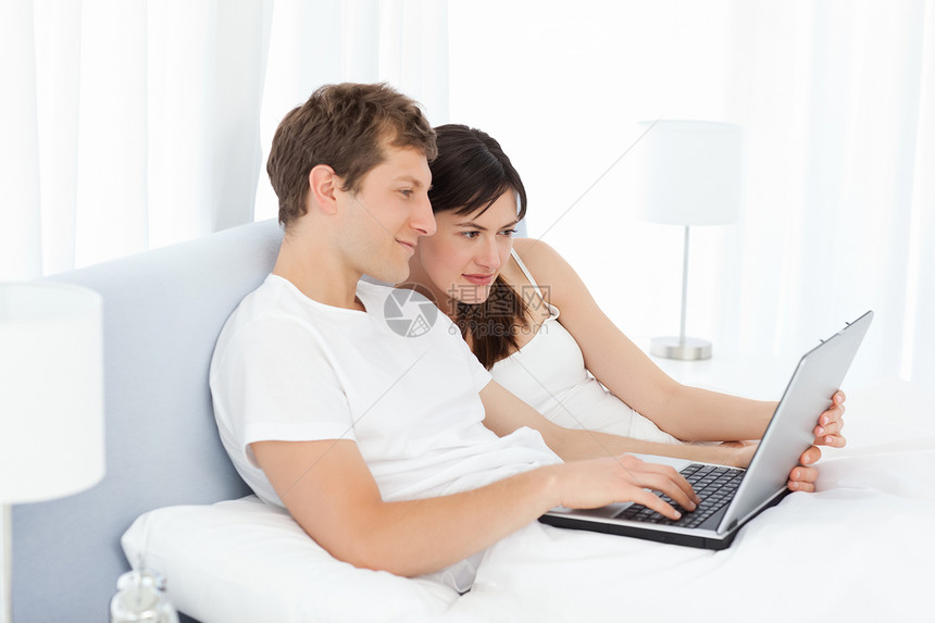 年轻夫妇在家电脑上观看视频的年青夫妇卧室女士女孩情人男生家庭幸福技术快乐笔记本图片
