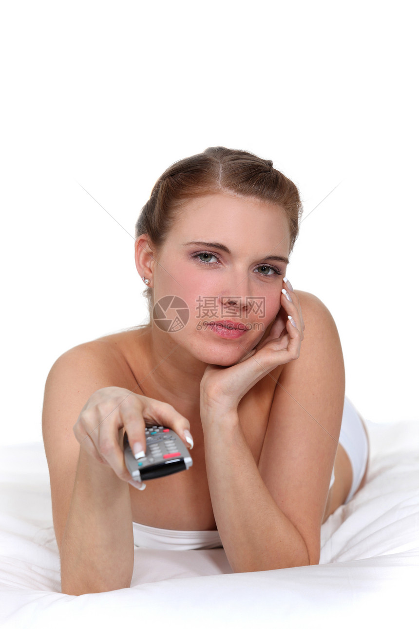 妇女躺在床上 并持有遥控器;图片