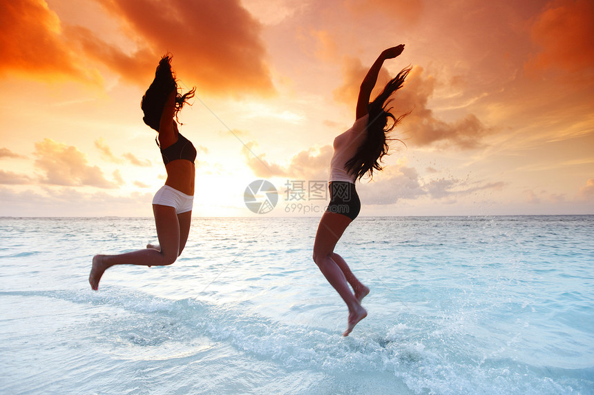 两个快乐的女人在海滩上跳跃行动活力女孩女性舞蹈海洋身体蓝色闲暇成人图片