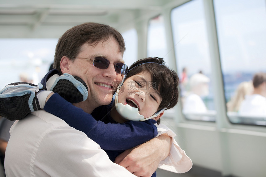 父亲在残疾儿子乘渡船时拥抱他们旅行孩子运输看门人混血微笑男生照顾者需求混血儿图片