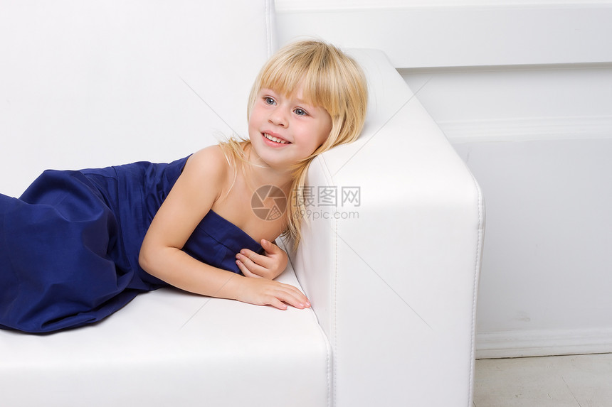 穿着蓝礼服的女孩 在白色沙发上头发工作室毛皮蓝色女性长椅休息女士金发女郎孩子图片