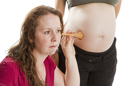 年轻助产士在孕妇肚子里倾听婴儿的心声背景图片