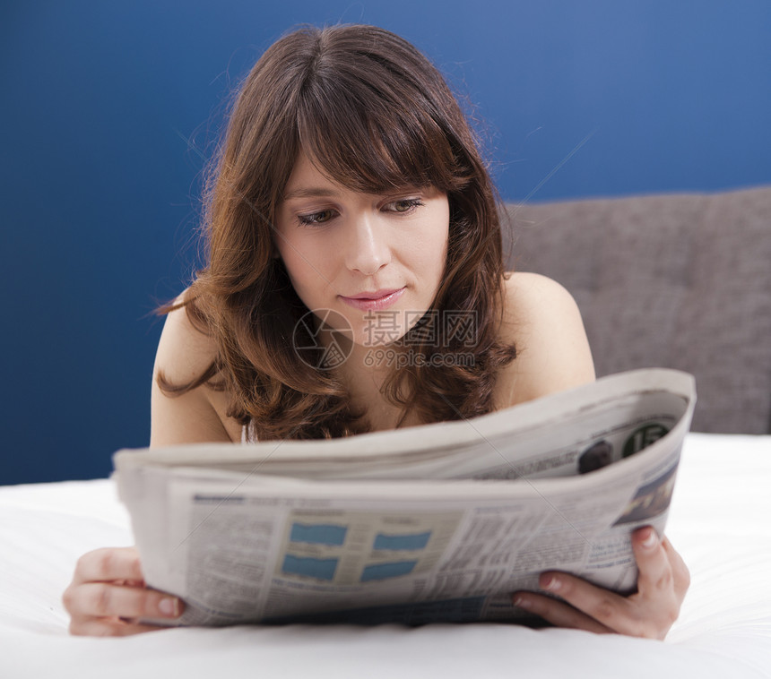 阅读报纸蓝色睡衣卧室说谎商业女性成人黑发白色房间图片