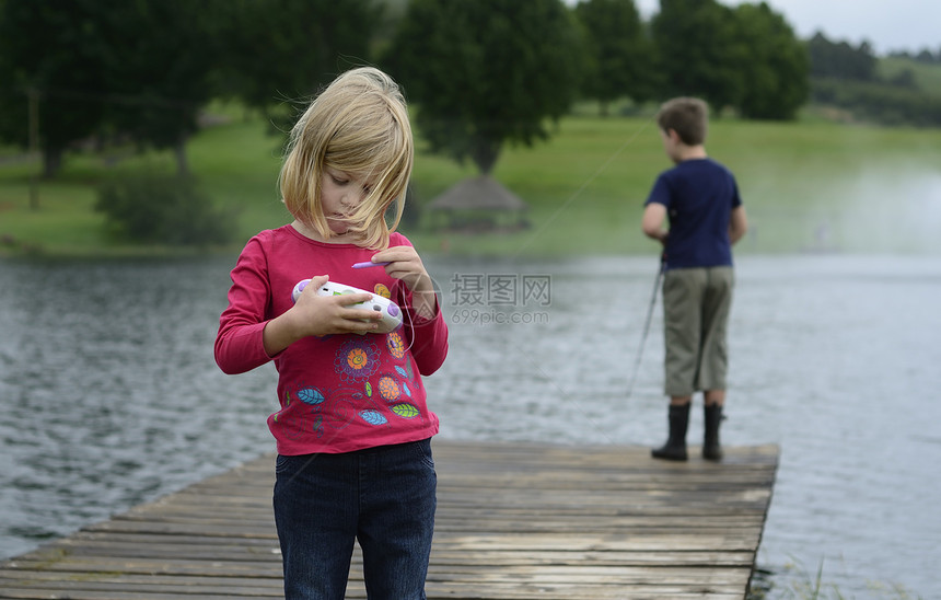 在大自然中玩电脑游戏的年轻女孩池塘家庭靴子爱好闲暇青年钓鱼码头渔夫娱乐图片