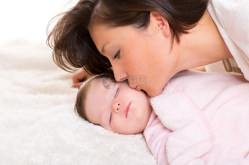 婴儿女孩和母亲亲吻她 快乐地躺在白衣上图片