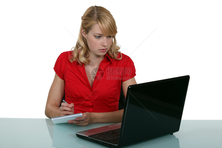 Blond秘书从笔记电脑屏幕上作笔记图片