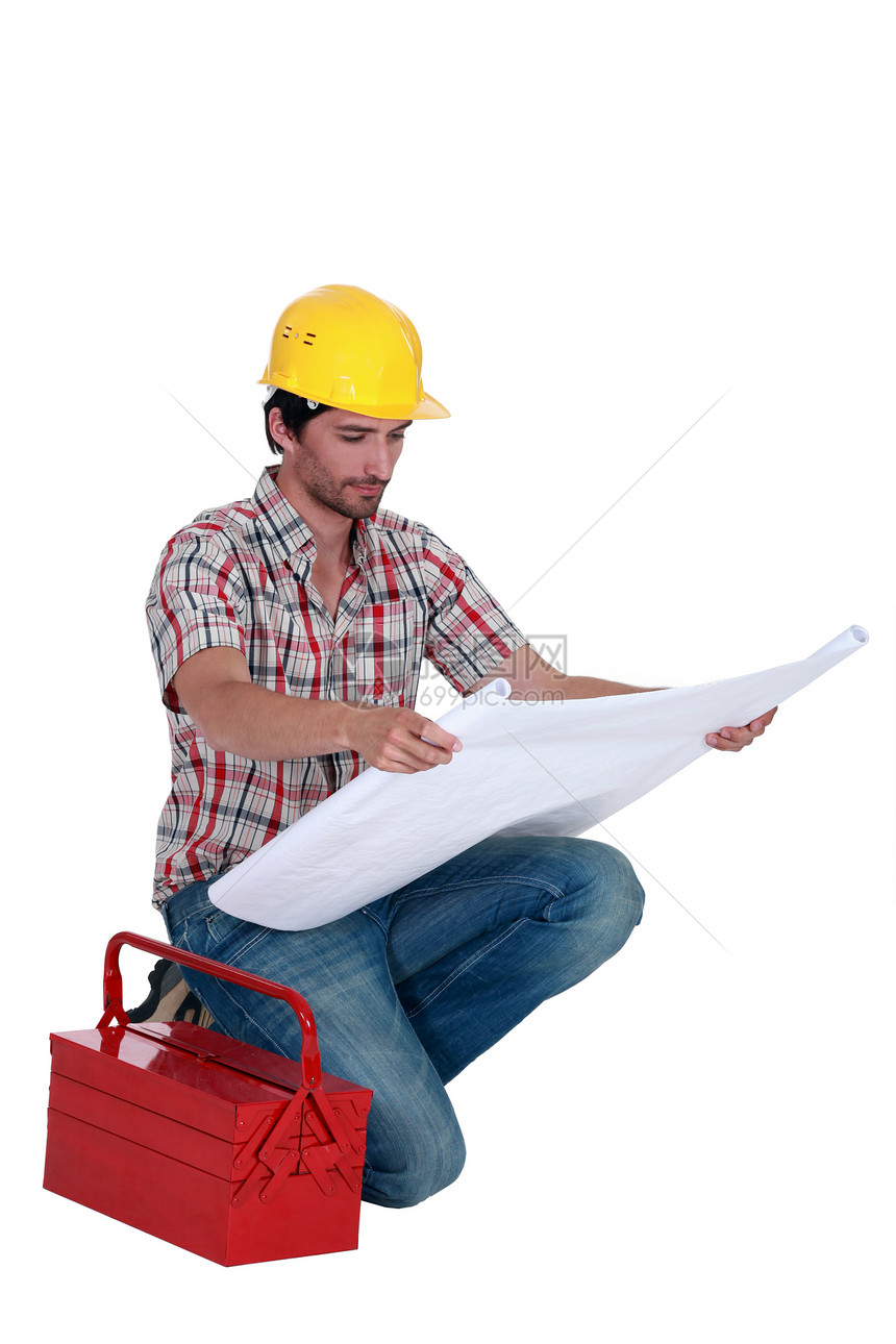 构建者在用工具箱跪下时阅读计划图片