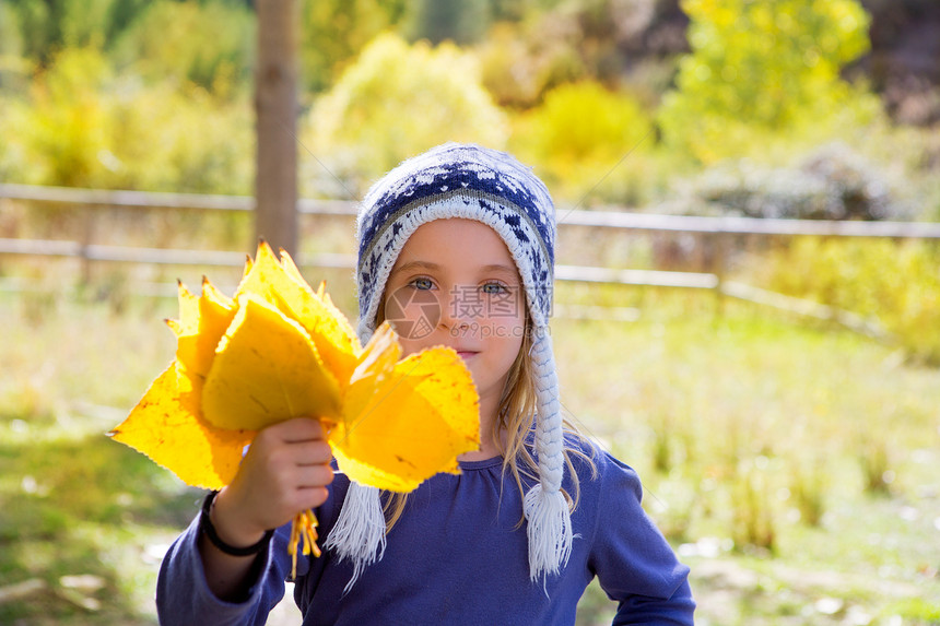 秋天的童女儿童 在阴花林中 黄色落叶手握着金发微笑童年树干眼睛公园花园树叶帽子蓝色图片
