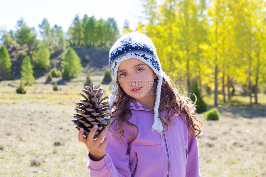 冬季秋天抱着松锥鱼的小女孩女孩羊毛季节外套帽子蓝色松树森林公园草地图片