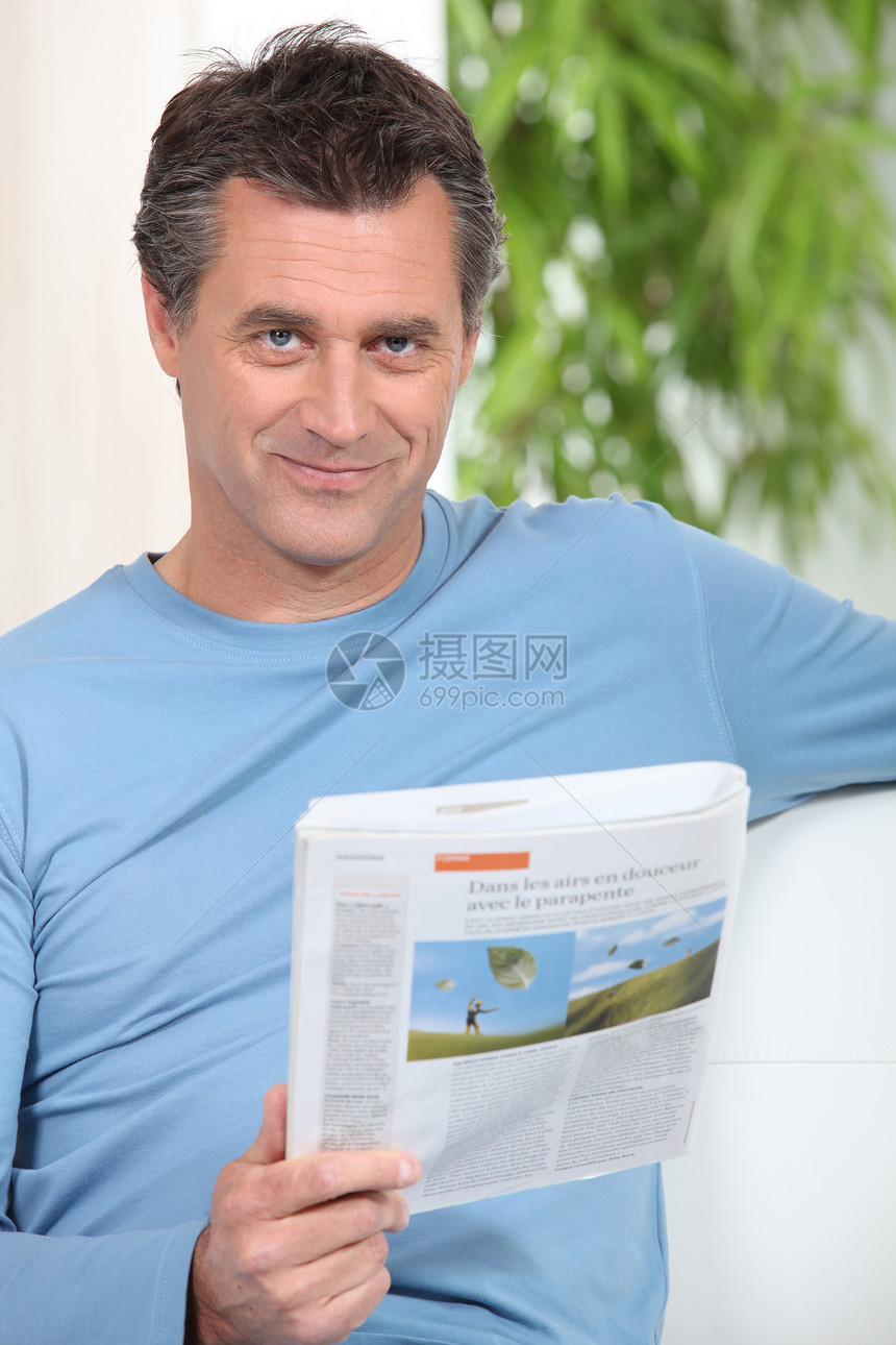 微笑的男人在沙发上读报纸图片