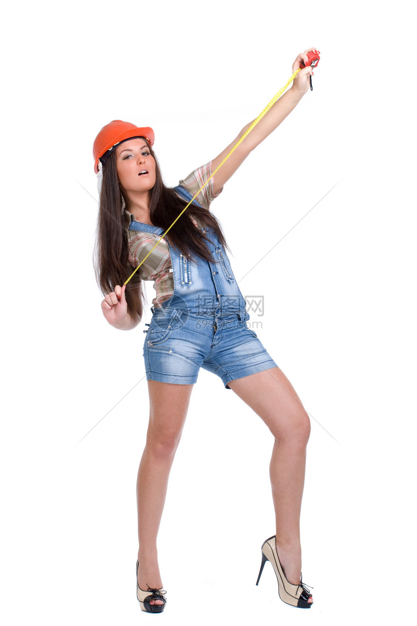 戴橙色头盔的年轻女子携带胶带深色手工具衬衫白色蓝色工作服卷尺建设者长发短裤图片