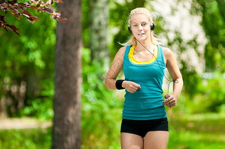 美丽的年轻女子在音乐上奔跑头发活力赛跑者女士运动员肌肉耳机运动公园跑步背景图片