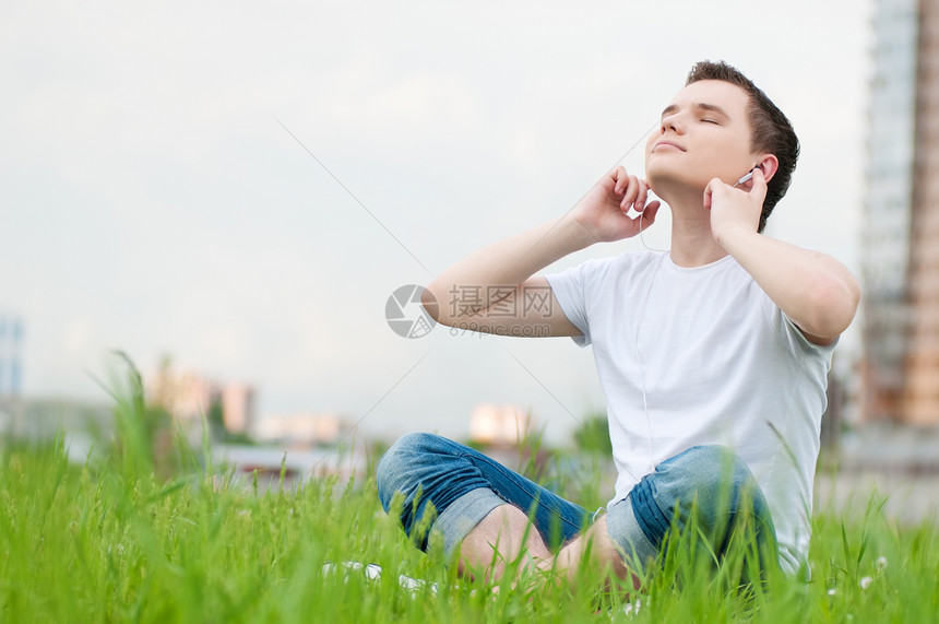 有耳机的有吸引力的年轻人快乐自由男性美丽男人天空公园音乐街道闲暇图片