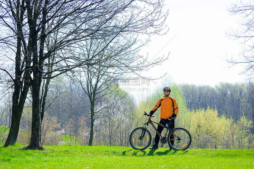 在绿草地上与他的Bike骑在绿草地上的自行车赛车员名单男人男性天空运动橙子头盔蓝色锻炼爬坡成人图片