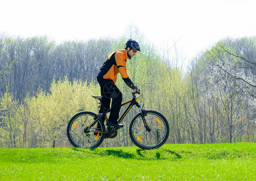 在绿草地上骑自行车的赛车女运动员娱乐成人乐趣下坡蓝色速度锻炼活动爬坡橙子图片