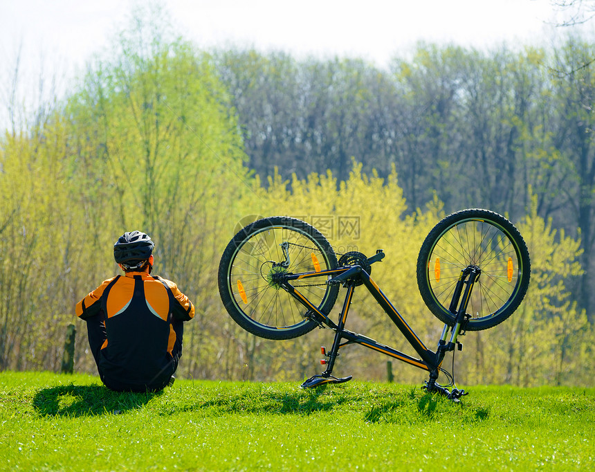 赛车手坐在靠近他自行车的草地上图片