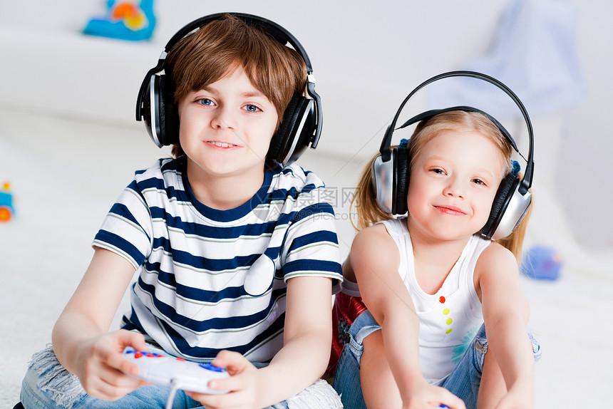 玩游戏控制台的可爱男孩女孩电子游戏地毯男性耳机团体女性微笑电脑孩子儿子图片