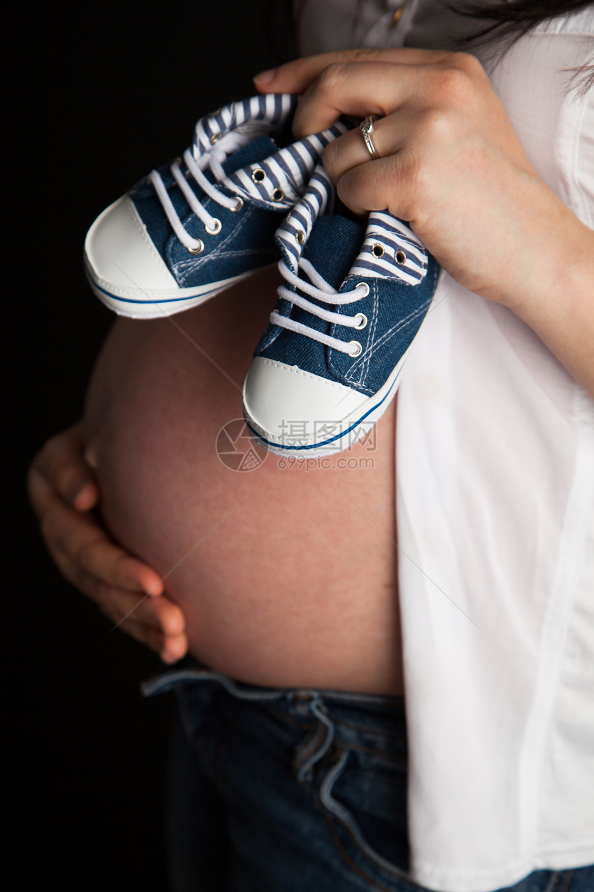 肚子上戴着一双婴儿鞋的怀孕妇女图片