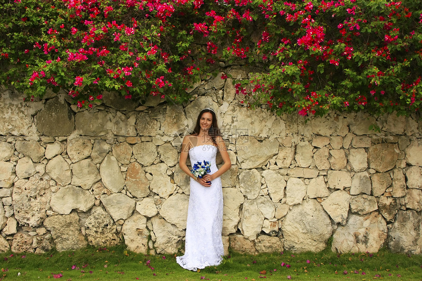 穿着婚纱的年轻女士 在石墙前摆着婚姻裙子花束订婚黑发冒充花朵未婚妻新娘微笑图片