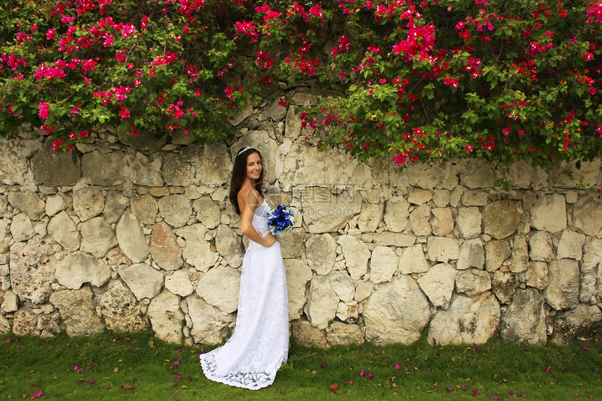 穿着婚纱的年轻女士 在石墙前摆着婚礼黑发微笑花朵头发花束订婚婚姻未婚妻女孩图片