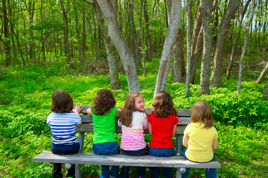坐在森林公园长椅上的儿童姊妹和朋友女孩学校假期丛林女孩们姐妹森林公园幸福家庭树干图片