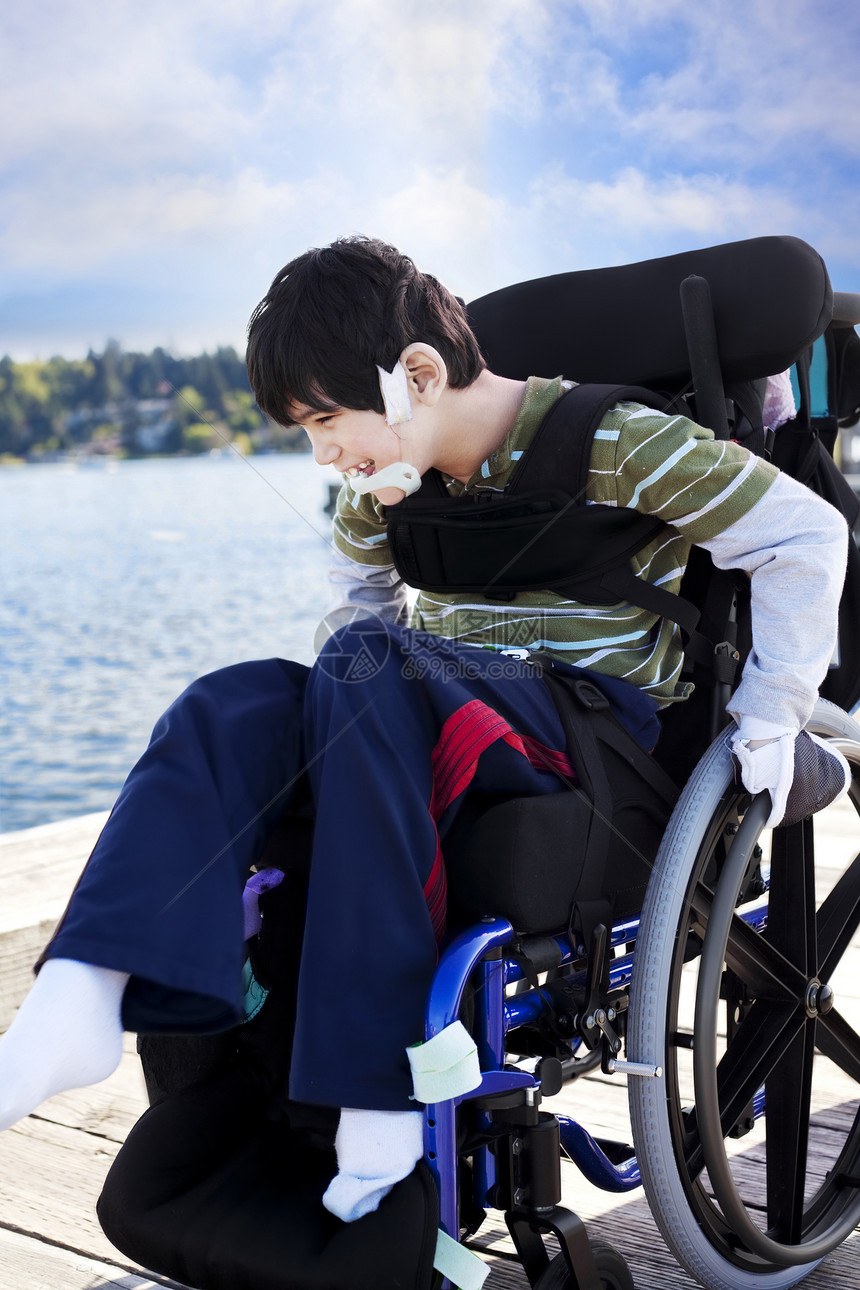 在湖边码头轮轮椅的残疾小男孩男性小朋友乐趣混血微笑医疗孩子蓝色晴天混血儿图片
