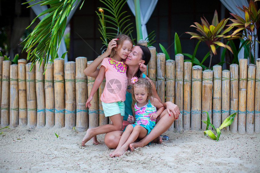 年轻母亲和两个美丽的女儿坐在栅栏附近的沙滩上 坐落在围栏旁的沙子上孩子旅游女士成人海滩婴儿海洋女孩海岸假期图片