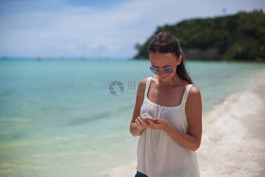 海滩上的年轻美女 在看她的电话时看着她的手机图片