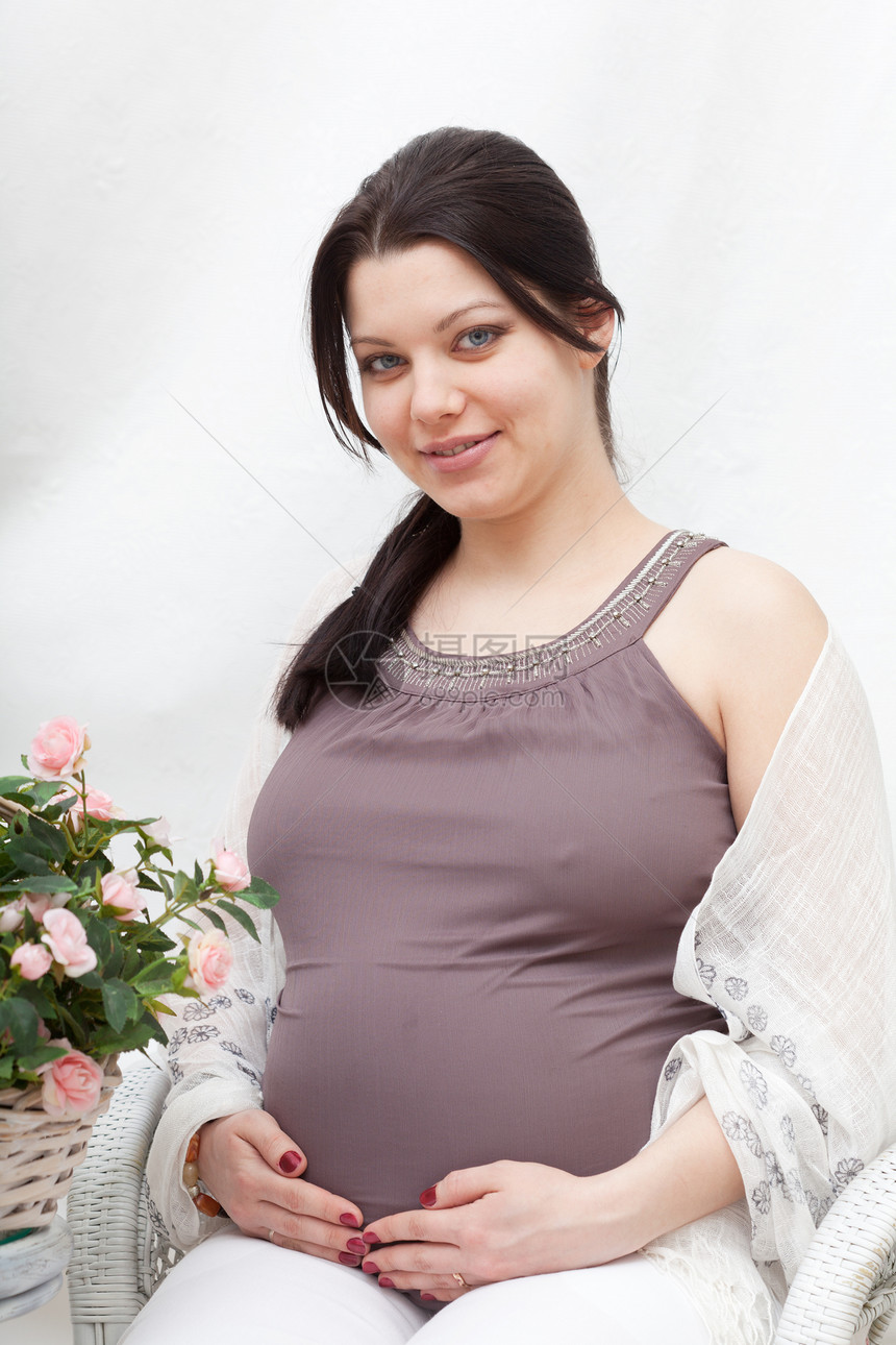 幸福的孕妇坐在房间里拿着鲜花坐着图片