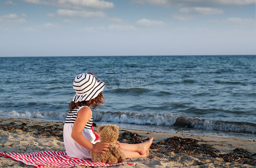 小女孩和泰迪熊坐在沙滩上图片
