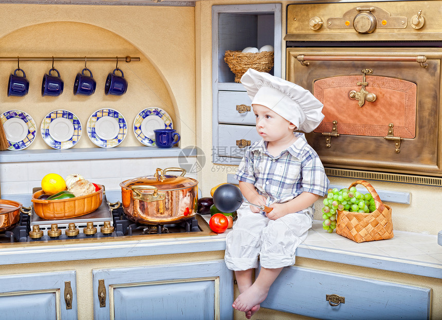 小男孩坐在厨房的桌子上 做厨师戏剧食物男生蔬菜童年女性火炉孩子平底锅帽子图片