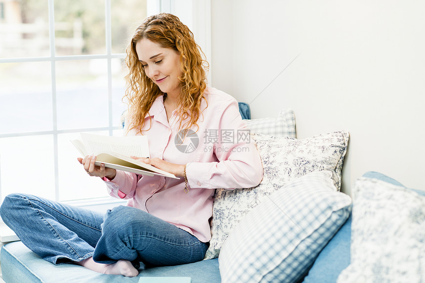 妇女按窗口阅读书幸福成人框架晴天沙发日光中年微笑靠垫房子图片