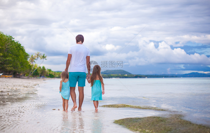 看着父亲和两个女儿在海边行走的近视图片