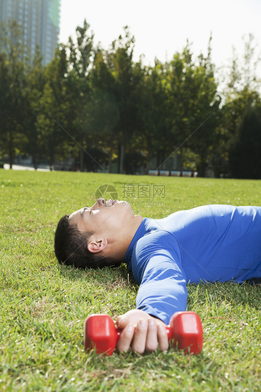年轻的运动健壮的年轻人躺在公园里 与哑巴一起 垂直图片