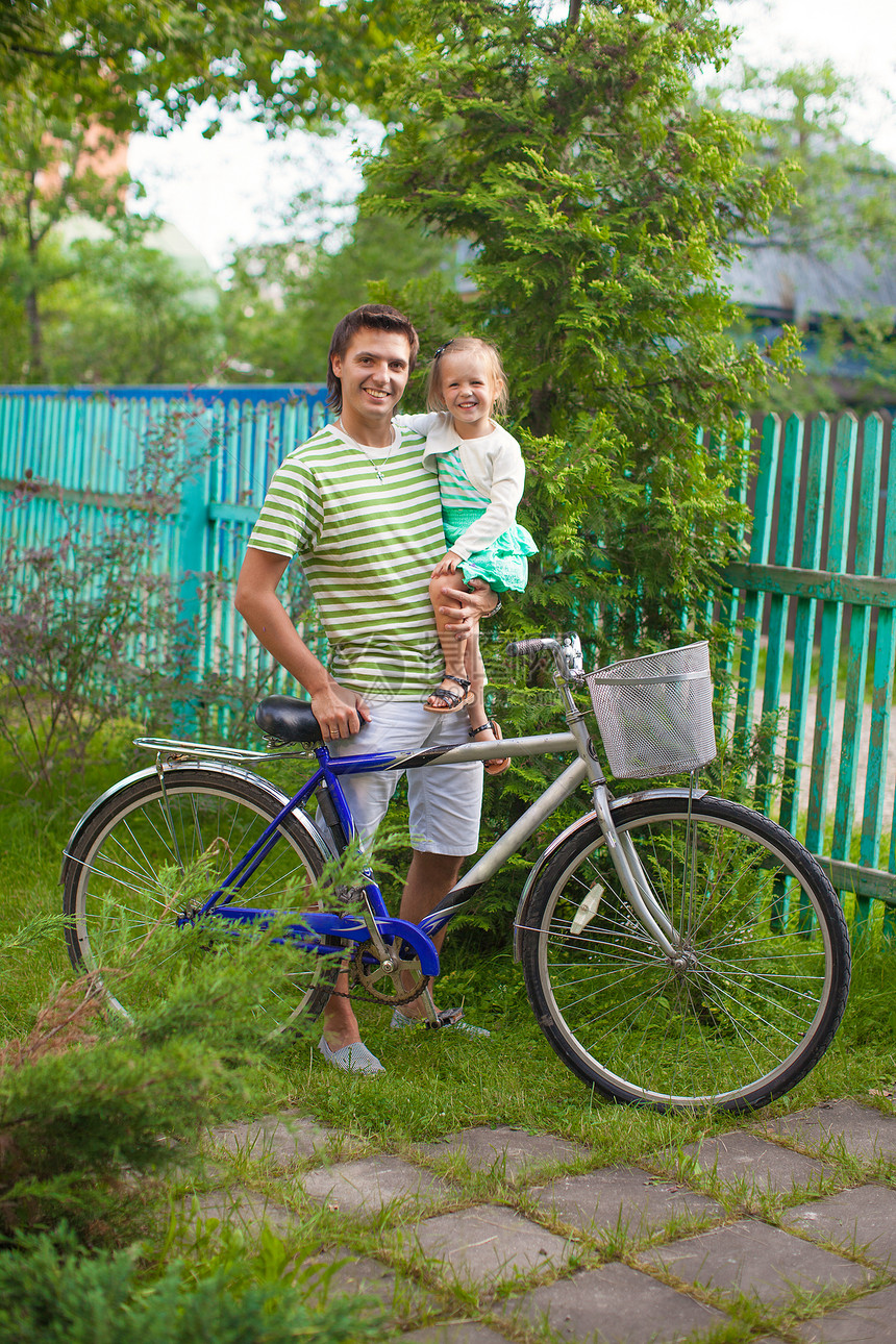 年幼的父亲和可爱的小女儿 在农舍周围骑自行车活动爸爸微笑家庭成人闲暇运动女孩骑术车轮图片