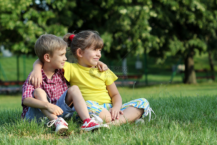 男孩和小女孩坐在公园的草地上图片