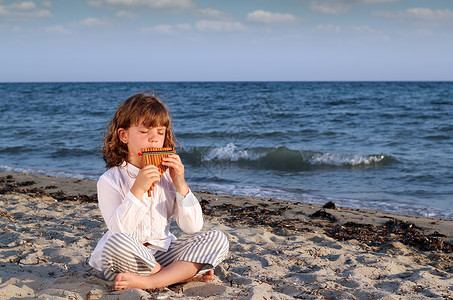 沙滩上音乐家美丽的小女孩坐在沙滩上玩锅炉管背景