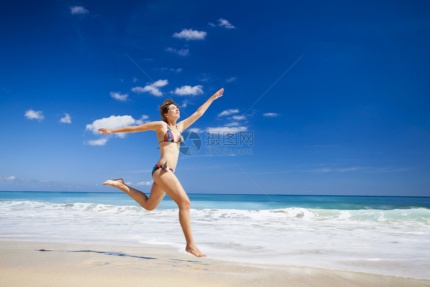 女人在海滩上跳跃女孩旅行蓝色游泳衣比基尼太阳海洋成人天堂跑步图片