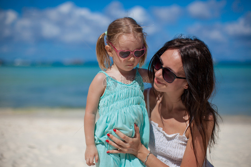 年轻美丽的母亲和她可爱的小女儿在热带海滩的肖像图片