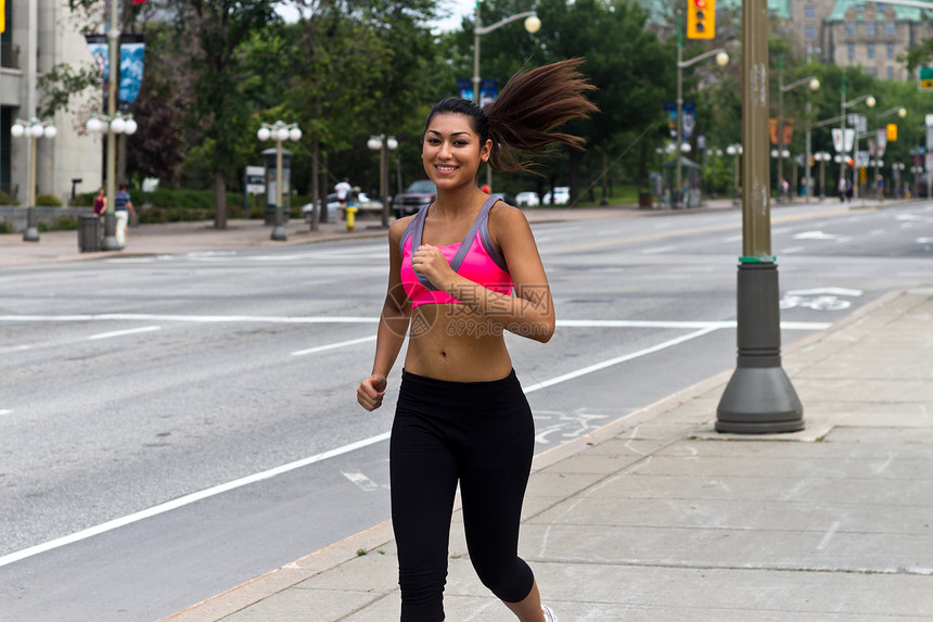 合适的年轻女子在繁忙的街道上奔跑速度慢跑者活力微笑城市福利运动女性成人文胸图片