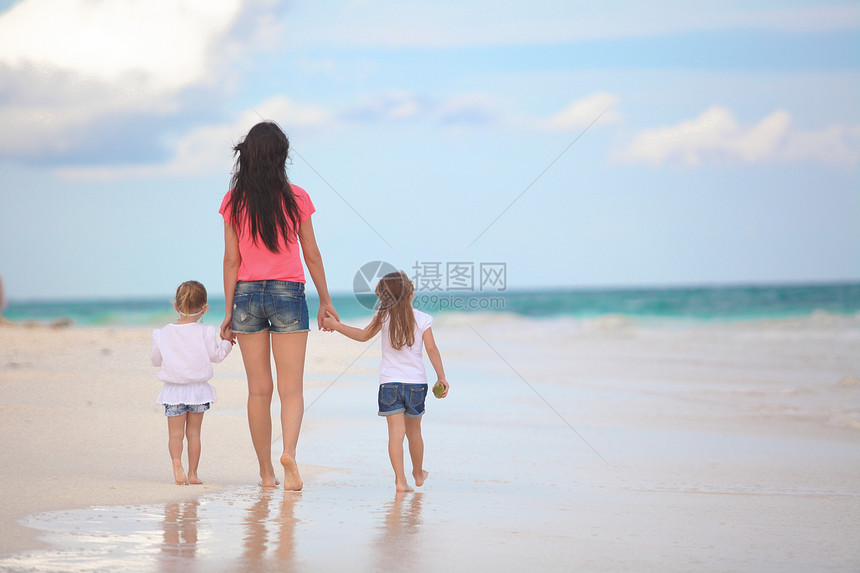 年轻母亲和可爱女儿在热带海滩散步的背面景象图片