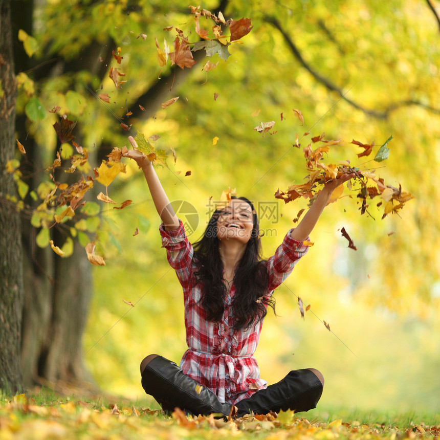 秋天公园的女子落叶木头假期微笑女性公园投掷头发喜悦季节成人图片