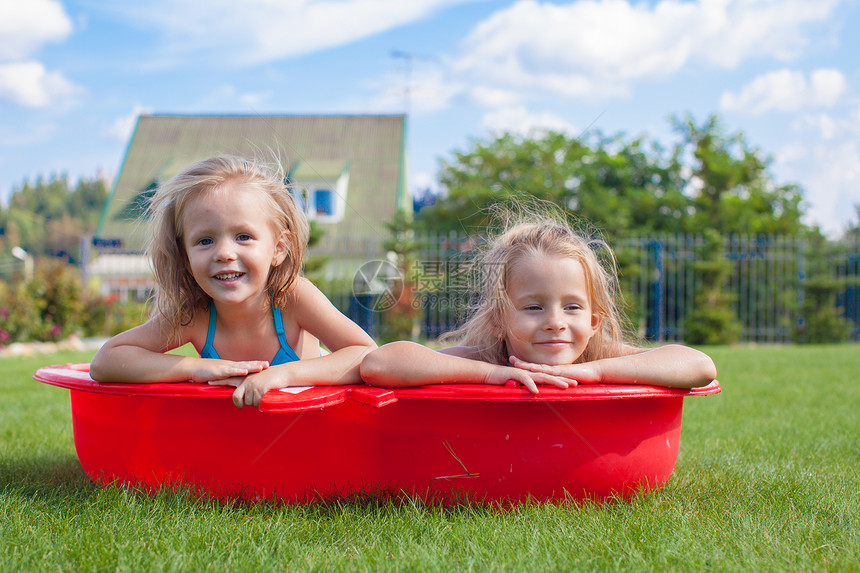 两个妹妹在小泳池里 玩耍和冲着院子里的花水享受水池喜悦运动闲暇软管晴天娱乐乐趣孩子图片