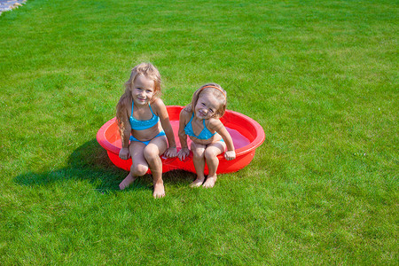 两个妹妹在小泳池里 玩耍和冲着院子里的花水女孩飞溅假期草地运动喜悦晴天花园微笑乐趣背景
